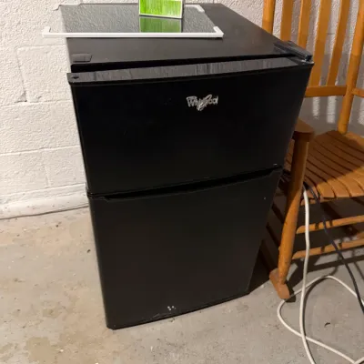 Sale Photo Thumbnail #236: Whirlpool black mini refrigerator with a separate freezer compartment, showing some minor wear.