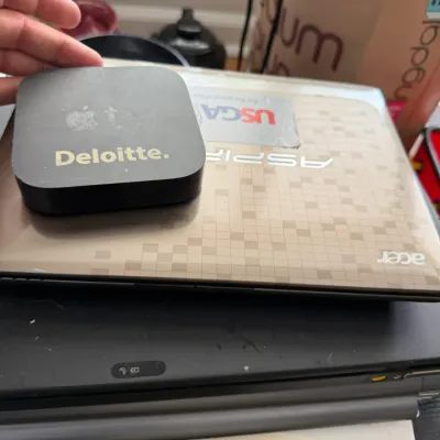 Apple TV media player with a Deloitte logo sticker, resting on top of an Acer Aspire laptop and another black laptop.