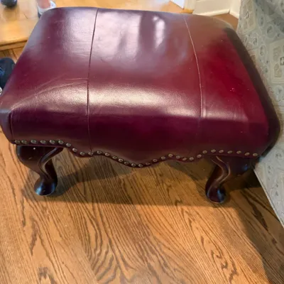 Traditional burgundy leather ottoman featuring brass nailhead trim and carved cabriole legs.