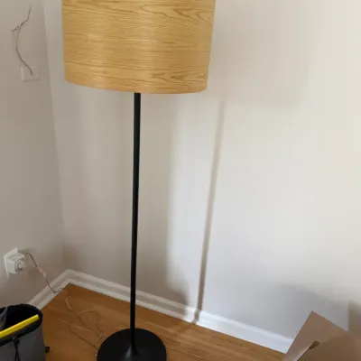 Modern floor lamp featuring a slender black metal pole and base, paired with a drum shade in a light wood grain finish.