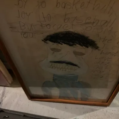 Sale Photo Thumbnail #222: Framed child's drawing and handwritten poem featuring a portrait of a man with a mustache, presented in a simple wooden frame.