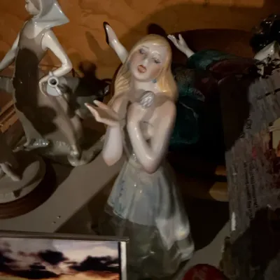 Sale Photo Thumbnail #176: Vintage Lladro-style porcelain figurine of a blonde woman in a flowing dress, displayed alongside other collectible figurines on a shelf.