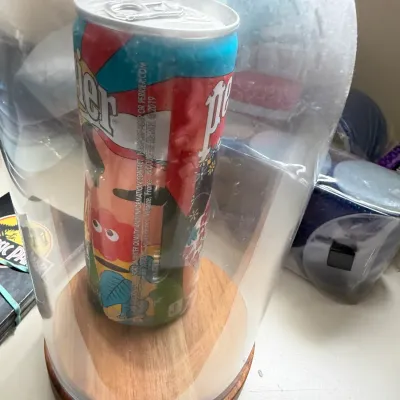 Limited edition Perrier slim can featuring colorful pop art graphics, displayed inside a glass cloche with a wooden base.