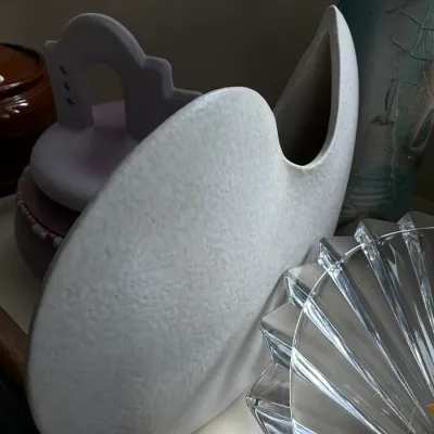 Postmodern white ceramic crescent vase with a textured finish, displayed alongside other decorative glassware and pottery.
