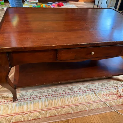 Traditional cherry-finished wood coffee table featuring a single drawer with a brass pull, a lower storage shelf, and curved cabriole...