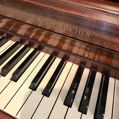 Carl Fischer upright piano featuring a mahogany wood finish and gold-lettered branding above the keyboard.