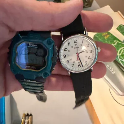 Sale Photo Thumbnail #159: Two wristwatches, including a teal and black Wilson digital sports watch and a classic Timex Indiglo analog watch with a white face and black strap.