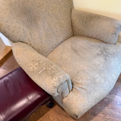 Traditional upholstered armchair with a beige geometric pattern, showing some wear on the seat and arms, pictured next to a burgundy...