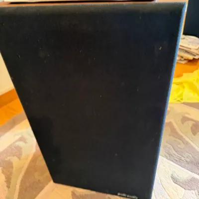 Vintage Polk Audio floor-standing speaker with a black fabric grille and wood-grain cabinet, showing some light wear.