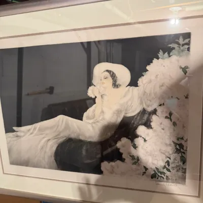 Sale Photo Thumbnail #179: Framed Art Deco style print by Louis Icart, depicting a reclining woman in a white gown and hat surrounded by white blossoms.
