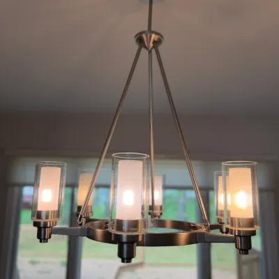 Modern brushed nickel chandelier featuring a circular frame with six lights, each enclosed in double-glass cylinder shades with frosted...