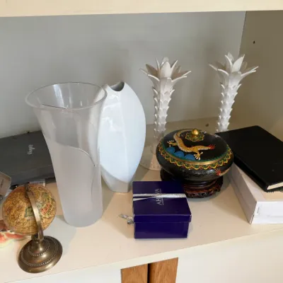 Sale Photo Thumbnail #104: Assorted home decor items on a shelf, including a frosted glass vase, a white ceramic vase, a pair of white candlestick holders, a small decorative globe, and a Chinese cloisonné lidded bowl.