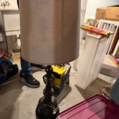 Sale Photo Thumbnail #171: Vintage table lamp featuring an ornate, dark metal filigree base and a tall, cylindrical beige fabric shade.