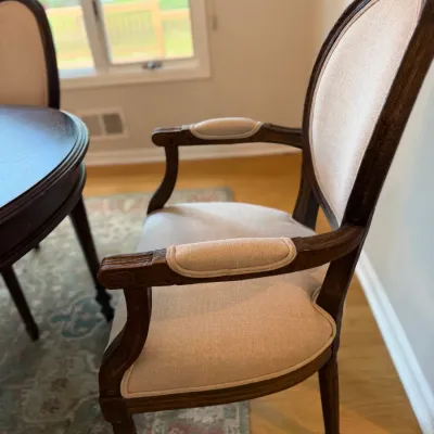 Louis XVI style armchair featuring a dark wood frame, oval back, and light beige upholstered seat, back, and armrests.