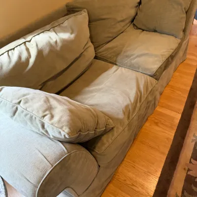 Contemporary two-cushion sofa with light olive green microfiber upholstery, rolled arms, and a skirted base.
