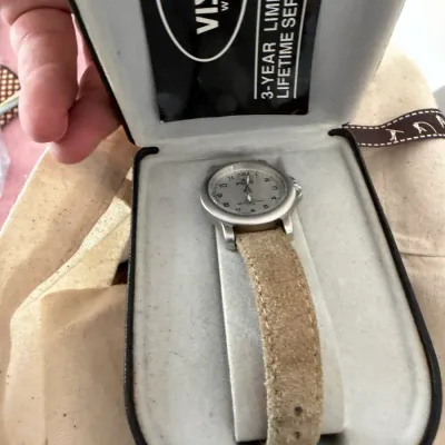Sale Photo Thumbnail #141: Visage watch with a silver-tone bezel and a textured tan suede strap, presented in its original branded display box.