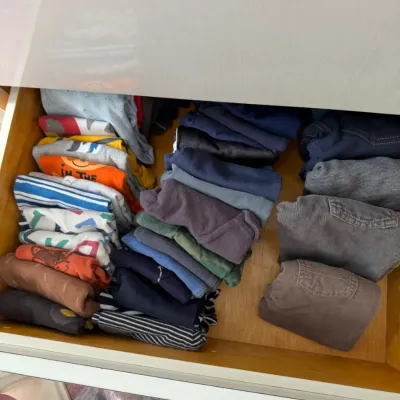Sale Photo Thumbnail #137: Assorted children's clothing, including folded shirts, pants, and shorts, organized inside a wooden dresser drawer.