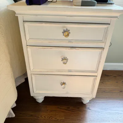 Sale Photo Thumbnail #150: White-painted three-drawer nightstand featuring decorative flower-shaped knobs and short turned feet.