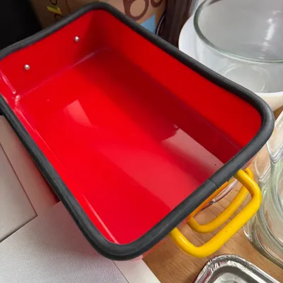 Vintage Copco red enamel roasting pan designed by Michael Lax, featuring a black rim and yellow loop handles.