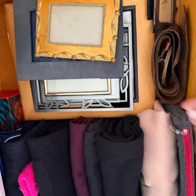 Sale Photo Thumbnail #121: Assorted picture frames, rolled clothing, a brown leather belt, and a small zippered pouch stored inside a wooden drawer.
