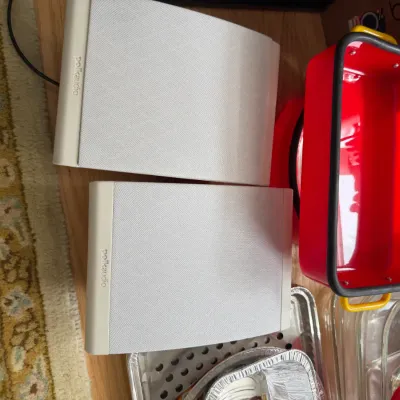 Pair of white Polk Audio bookshelf speakers, shown alongside a red and yellow rectangular baking dish and other kitchenware.