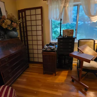 Eclectic room featuring a vintage mahogany slant-front desk, a wooden shoji screen, a tall black chest of drawers, and an upholstered...