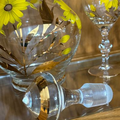 Sale Photo Thumbnail #74: A beautiful mid-century vintage glassware set featuring a hand-painted yellow daisy and gold leaf design with gold-gilded rims. This 7-piece set includes one handled decanter pitcher, a matching glass stopper with a frosted ground base, and six coordinati