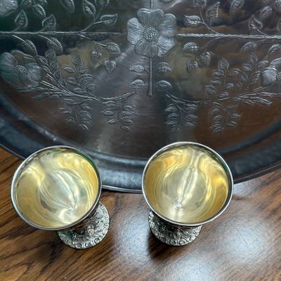 Sale Photo Thumbnail #69: A pair of vintage silver-plated goblets featuring an ornate, high-relief design of cherubs, grapevines, and musical instruments. The interiors are finished with a gold-tone wash. Each goblet stands approximately 5.5 inches tall. Shows light vintage wear a
