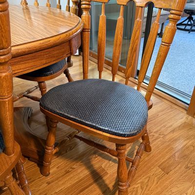 Sale Photo Thumbnail #83: A classic oak dining set featuring an oval pedestal table, two matching expansion leaves, and six spindle-back chairs. The chairs are upholstered in a dark blue textured fabric. The set shows light wear consistent with gentle use, with a clean finish on t