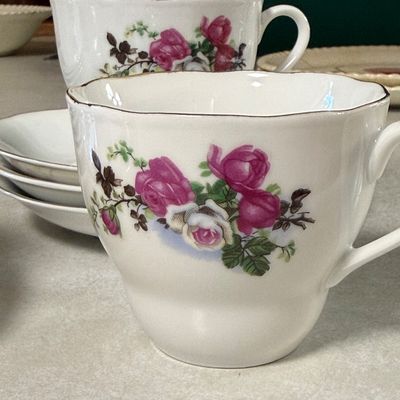 Sale Photo Thumbnail #87: A mixed ceramic set featuring four tea cups marked "Made in China" and a collection of matching saucers and side plates. The side plates are marked "JB Johnson Brothers Made in England Ironstone 3 A". All pieces feature a matching pink and white rose flor
