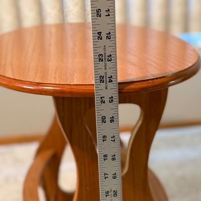 Sale Photo Thumbnail #79: A vintage wooden accent side table featuring an oval top, decorative cutout side panels, and a lower spindle-railed shelf designed to hold magazines or books. Constructed from wood with a warm honey oak finish. Shows minor surface wear, light scratches, a