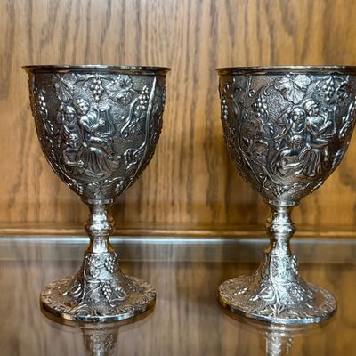 Sale Photo Thumbnail #68: A pair of vintage silver-plated goblets featuring an ornate, high-relief design of cherubs, grapevines, and musical instruments. The interiors are finished with a gold-tone wash. Each goblet stands approximately 5.5 inches tall. Shows light vintage wear a