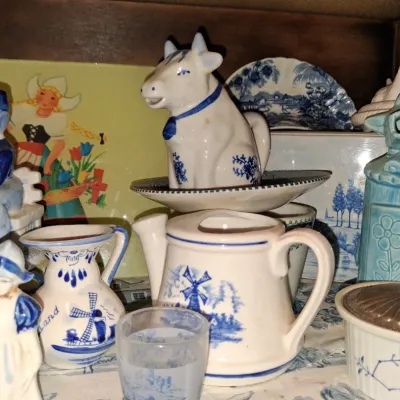 Sale Photo Thumbnail #63: Collection of Delftware and Dutch-themed ceramic collectibles, including a cow creamer, windmill pitchers, and traditional figurines.