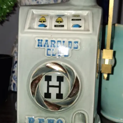Sale Photo Thumbnail #133: Vintage Jim Beam bourbon whiskey decanter shaped like a Harold's Club Reno slot machine, featuring a ceramic body with a gold-tone pull lever.