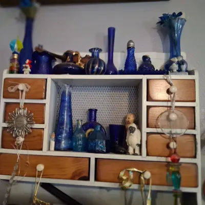 Sale Photo Thumbnail #93: Vintage white-painted wooden spice cabinet with natural wood drawers, filled with a collection of cobalt blue glass bottles, vases, and small figurines.