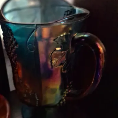 Sale Photo Thumbnail #109: Vintage blue carnival glass pitcher featuring an iridescent finish and embossed grape and leaf motif.