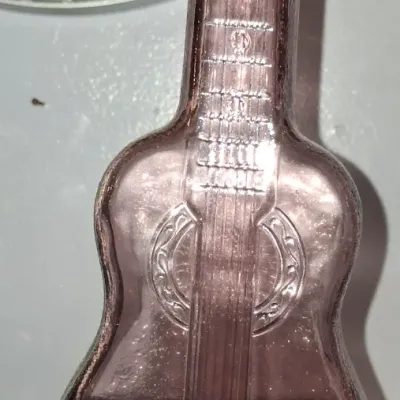 Sale Photo Thumbnail #131: Vintage amethyst glass bottle shaped like a guitar, featuring molded details of strings, frets, and a soundhole.