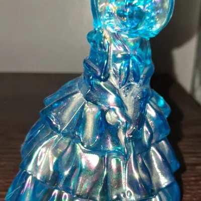 Sale Photo Thumbnail #127: Vintage Fenton blue iridescent carnival glass Southern Belle figurine, featuring a ruffled dress and bonnet.