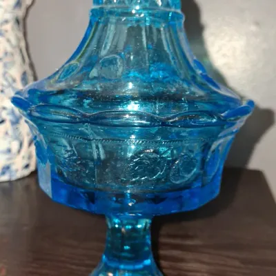 Sale Photo Thumbnail #120: Vintage blue pressed glass pedestal candy dish with a matching pointed lid, featuring embossed floral and geometric patterns.