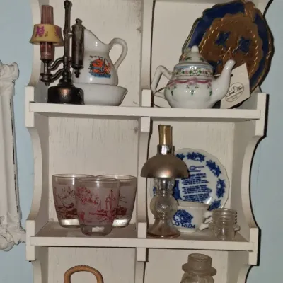 Sale Photo Thumbnail #53: Vintage white wooden wall shelf filled with various miniature collectibles, including small teapots, souvenir glasses, decorative plates, and a glass dog figurine.
