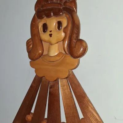 Sale Photo Thumbnail #52: Vintage mid-century wooden wall rack featuring a carved girl's face and hair bow, with fan-shaped slats and pegs for hanging items.