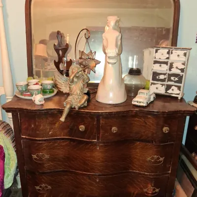 Sale Photo Thumbnail #45: Antique tiger oak serpentine dresser with matching mirror, displaying various decorative items including a ceramic horse head bust, angel figurine, and miniature chest of drawers.