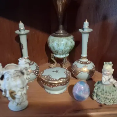 Sale Photo Thumbnail #102: Collection of vintage decorative items, including a pair of light green and gold porcelain decanters, a matching lidded trinket box, a small figurine, and two miniature brass oil lamps.