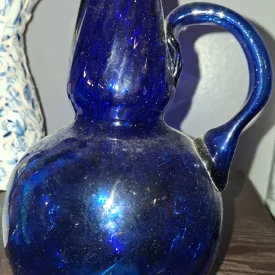 Sale Photo Thumbnail #123: Cobalt blue hand-blown art glass pitcher with a bulbous body, tapered neck, and applied handle.