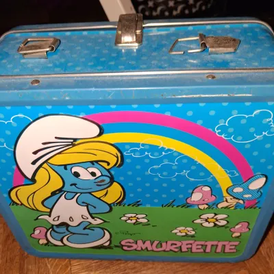 Sale Photo Thumbnail #137: Vintage 1982 Smurfette metal lunchbox by Aladdin, featuring colorful graphics of Smurfette, a rainbow, and mushrooms on a blue polka-dot background.