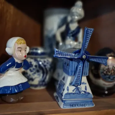 Sale Photo Thumbnail #103: Collection of Dutch-themed ceramic figurines, including a blue and white Delftware windmill marked 'Holland' and a small figurine of a girl in traditional Dutch attire.