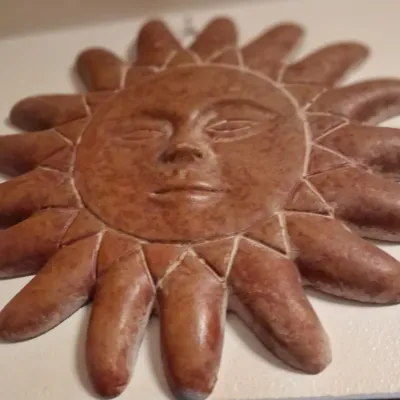 Sale Photo Thumbnail #86: Southwestern-style carved stone or clay sun face wall plaque with a mottled reddish-brown finish.