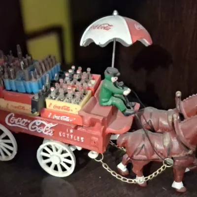 Sale Photo Thumbnail #111: Vintage cast iron Coca-Cola horse-drawn delivery wagon toy, featuring two horses, a driver under a branded umbrella, and miniature crates of soda bottles.