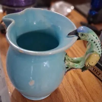 Sale Photo Thumbnail #106: Vintage light blue ceramic pitcher featuring a colorful parrot-shaped handle, showing minor wear and glaze imperfections.
