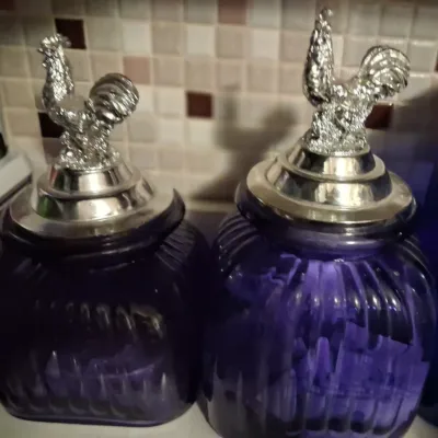 Sale Photo Thumbnail #78: Pair of ribbed purple glass canisters featuring silver-tone metal lids topped with detailed rooster finials.